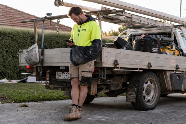 Australian sole-trader tradie beside his ute comparing job-management apps on his phone